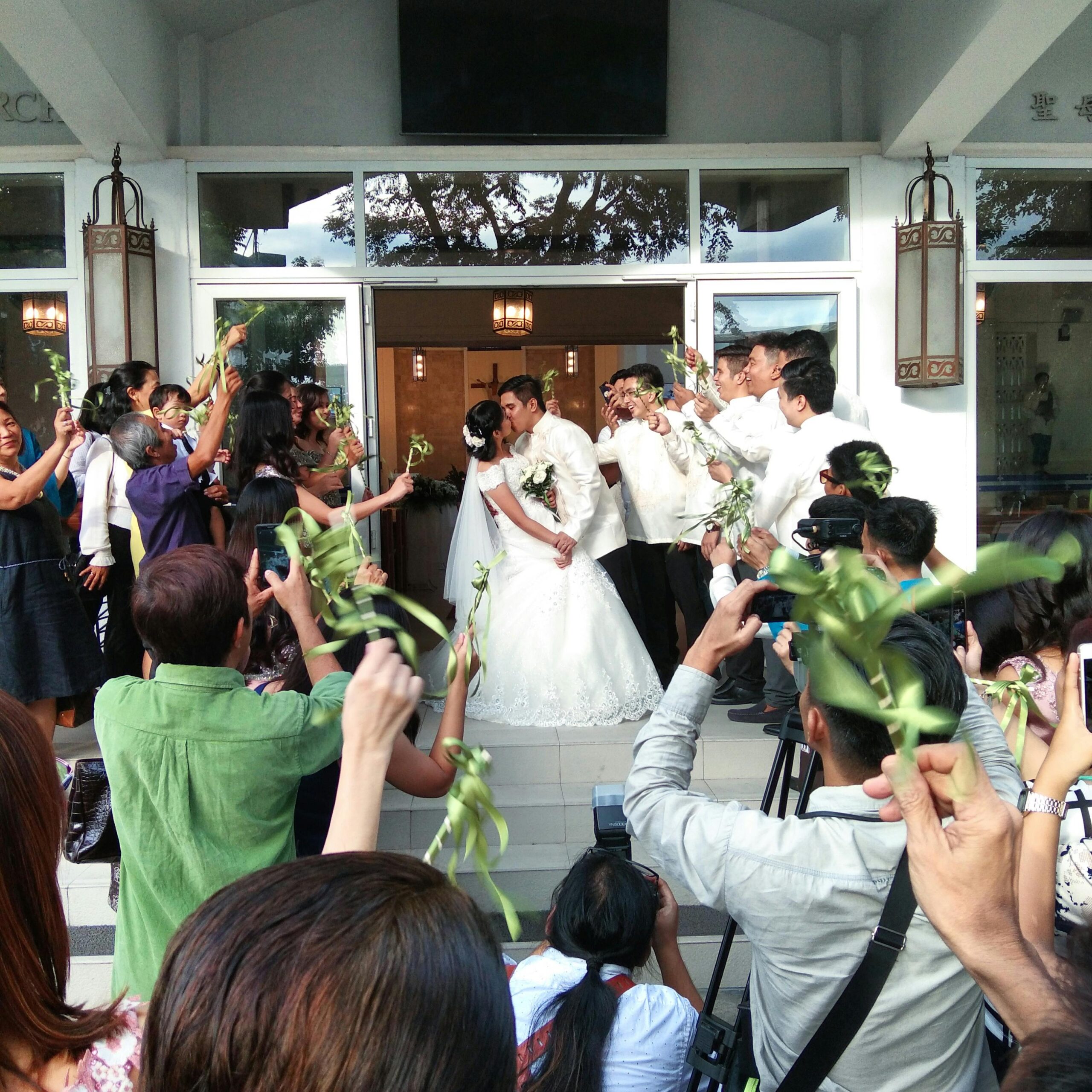 Bride and groom sharing a kiss surrounded by happy guests at their wedding celebration.